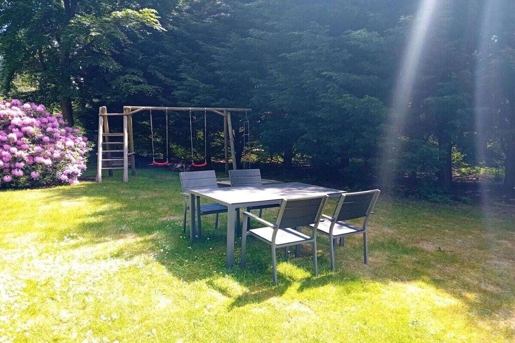 An outdoor seating area with a table and chairs, a swing set, and a garden with flowers.