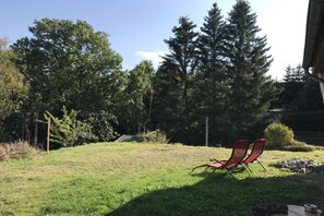A grassy backyard with two red lawn chairs and a stone wall. - Holiday home in Stiege with barbecue (Stiege)