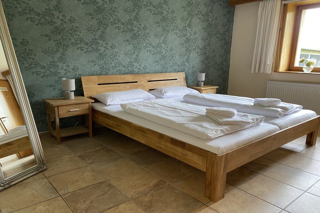 Una cama bien hecha con sábanas blancas, cabecera de madera y dos mesitas de noche con lámparas.