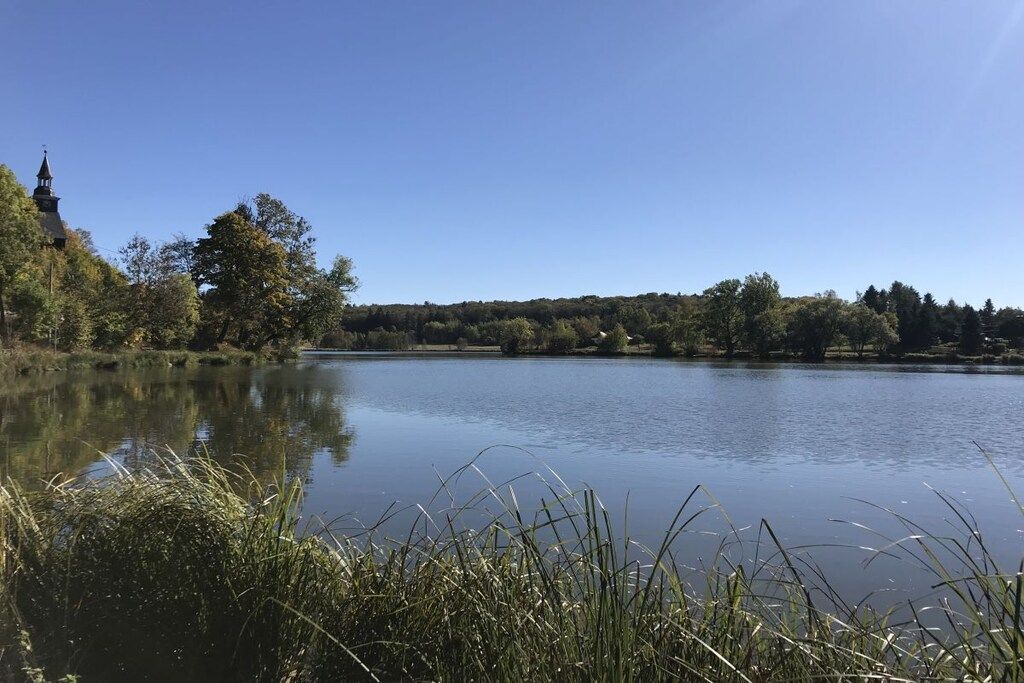 Un lago tranquilo con la aguja de una iglesia a la izquierda, rodeado de árboles y vegetación.