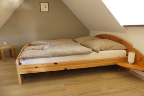 Ein Einzelbett mit Holzrahmen, ein kleiner Nachttisch und ein Beistelltisch in einem Zimmer mit schrägen Wänden und Holzboden.