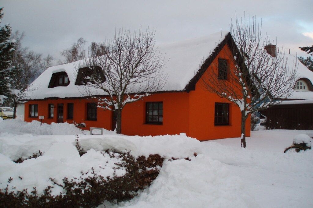 Une maison à deux étages, dotée d’un toit à forte pente recouvert de neige, et entourée d’un paysage enneigé.