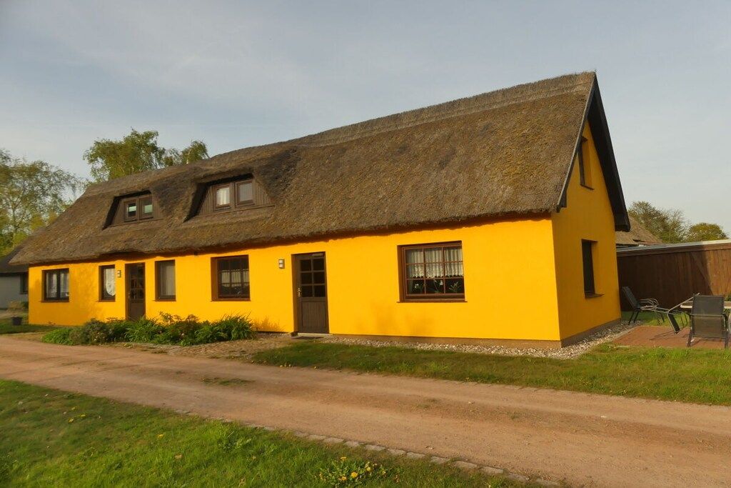 Un bâtiment jaune avec un toit de chaume, un petit porche et une seule porte.