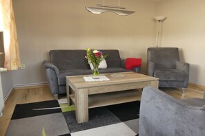 Ein Wohnzimmer mit grauem Sofa, einem grauen Sessel, einem Holztisch mit Blumenvase und einer modernen Lampe.