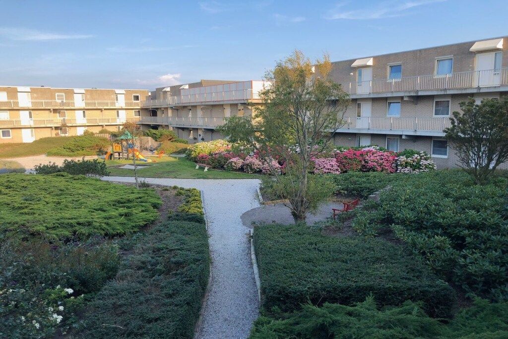 Een woongebouw met een centrale binnenplaats, een speeltuin en diverse beplanting.