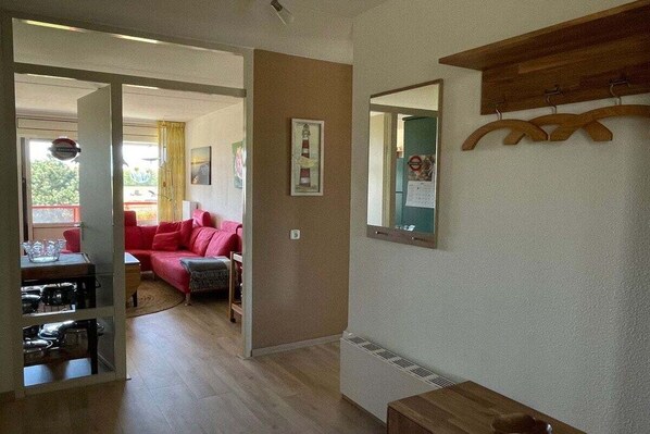 Ein Zimmer mit einem roten Sofa, einem Holztisch, einem Spiegel und einer Tür zu einem anderen Raum.