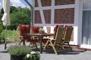 An outdoor patio with a brick wall, a wooden table, and four chairs. - Cieslik holiday half-timbered house (Hollern-Twielenfleth)