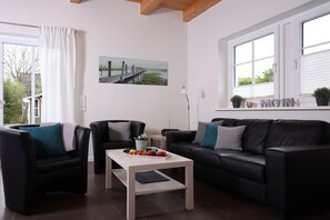 A modern living room with a sofa, armchairs, a coffee table, and a painting on the wall. - Cieslik holiday half-timbered house (Hollern-Twielenfleth)