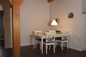 A dining area with a white table and chairs, a hanging light fixture, and a door in the background. - Cieslik holiday half-timbered house (Hollern-Twielenfleth)