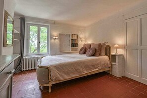 A bedroom with a bed, bedside lamps, a radiator, a window, and a bookshelf.