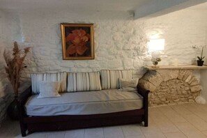 A cozy room with a stone wall, a wooden sofa with striped cushions, a framed painting, and a small table with decorative items.