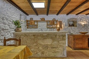 A rustic room with stone walls, wooden beams, a stone fireplace, and a wooden table with a yellow tablecloth.