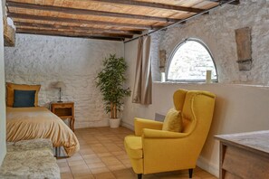 A room with a bed, a yellow armchair, a small table, a potted plant, and a window with a view.