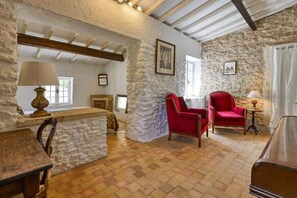A rustic room with stone walls, a wooden ceiling, a fireplace, and two red chairs.