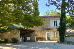 A stone building with a tiled roof, a covered outdoor seating area, and a gravel driveway.