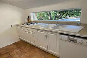 A kitchen with a gas stove, double sink, dishwasher, and a window with a view of trees.