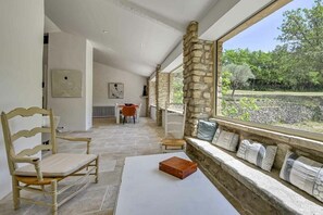 A room with a stone wall, a window seat with cushions, a table, and a chair.