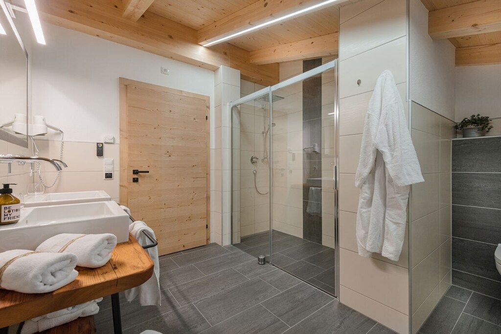 A modern bathroom with a wooden ceiling, a glass shower enclosure, and a sink with towels.