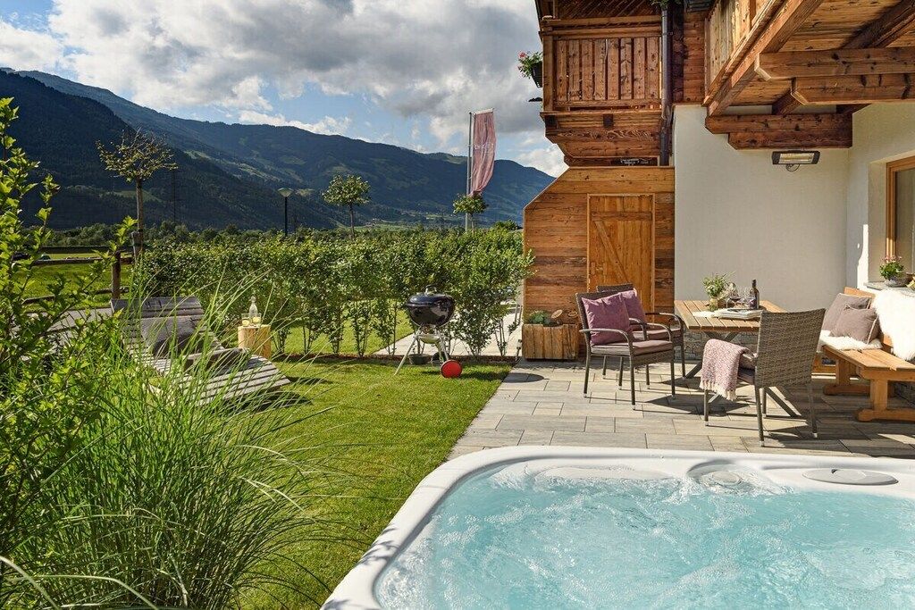 A hot tub with a wooden deck, outdoor seating, and a view of mountains.