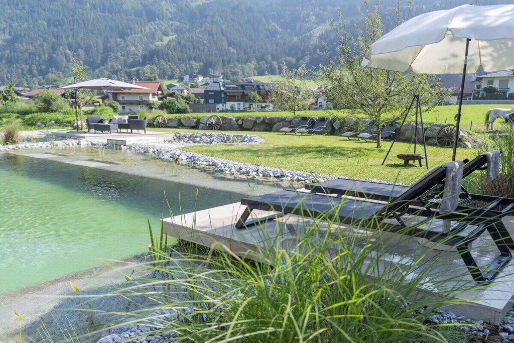 Ein ruhiger Poolbereich im Freien mit Liegestühlen, einem Kiesweg und Blick auf ein Bergdorf im Hintergrund.