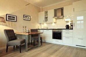 A modern kitchen with white cabinetry, a dining table with two chairs, and a coffee maker. - Villa Käthe "Apartment - 6b" (Kühlungsborn)