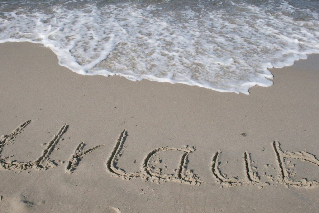 Une plage où le mot « LAUBA » est écrit dans le sable, des vagues qui s’approchent et un ciel dégagé.