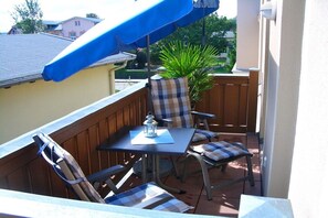 Ein Balkon mit Tisch und Stühlen, einem Blumentopf und einem blauen Sonnensegel.
