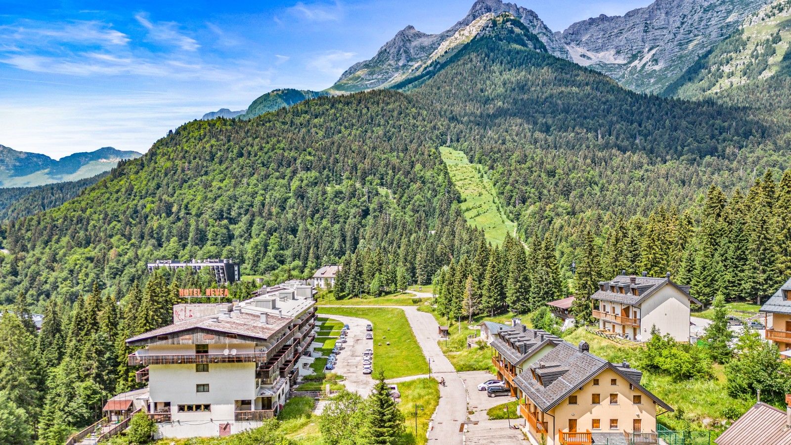 A hotel with multiple floors, a parking lot, and a view of a mountainous landscape.