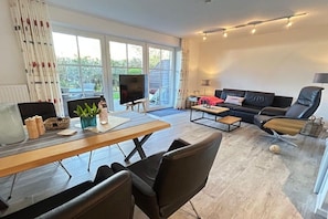Ein modernes Wohnzimmer mit Fernseher, Sofa und Essbereich.