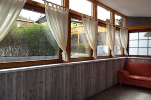 Ein Zimmer mit großen Fenstern, einer Holzwand und einem roten Sofa.