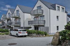 A modern residential building with multiple balconies, a white exterior, and a parked car. - Holiday apartment with 2 bedrooms (Rantum)