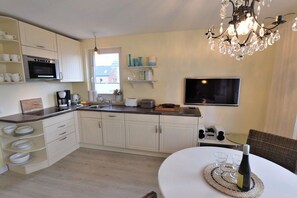 A modern kitchen with white cabinets, a built-in oven, a coffee maker, and a dining area with a table and chairs. - Holiday apartment with 2 bedrooms (Rantum)