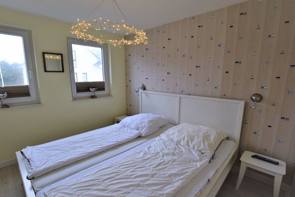 Une chambre avec deux lits jumeaux, une tête de lit blanche, une table de chevet et un luminaire suspendu.