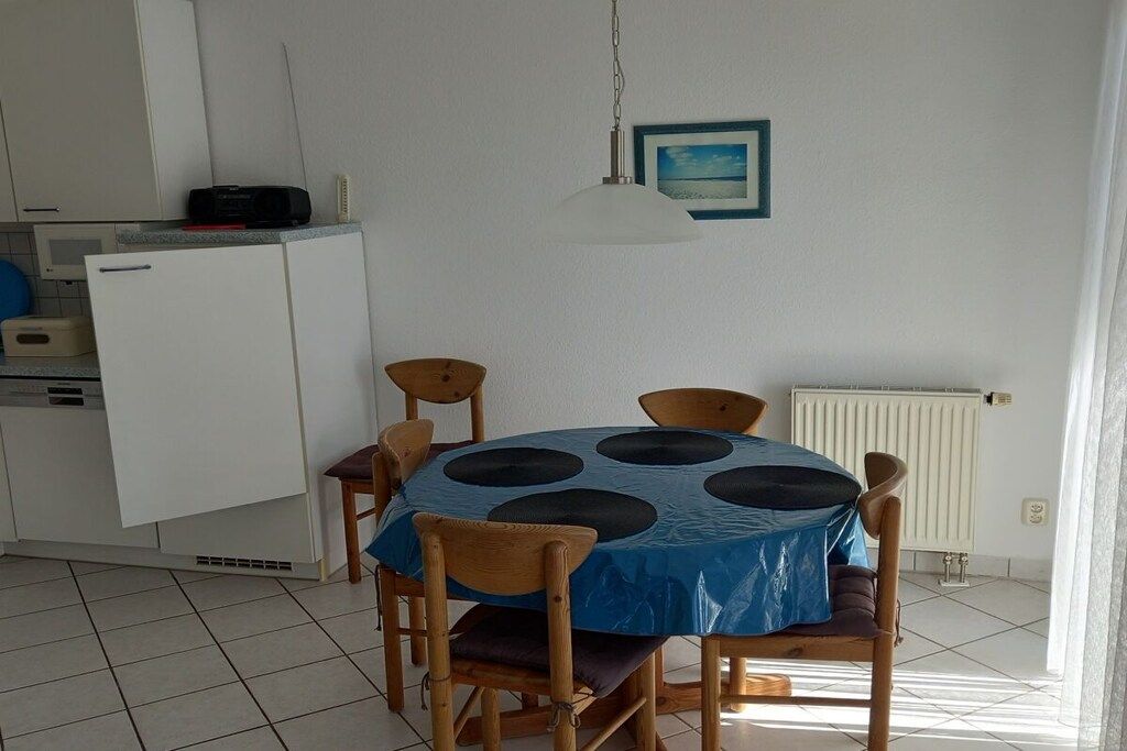 A dining area with a round table covered by a blue tablecloth, surrounded by wooden chairs.