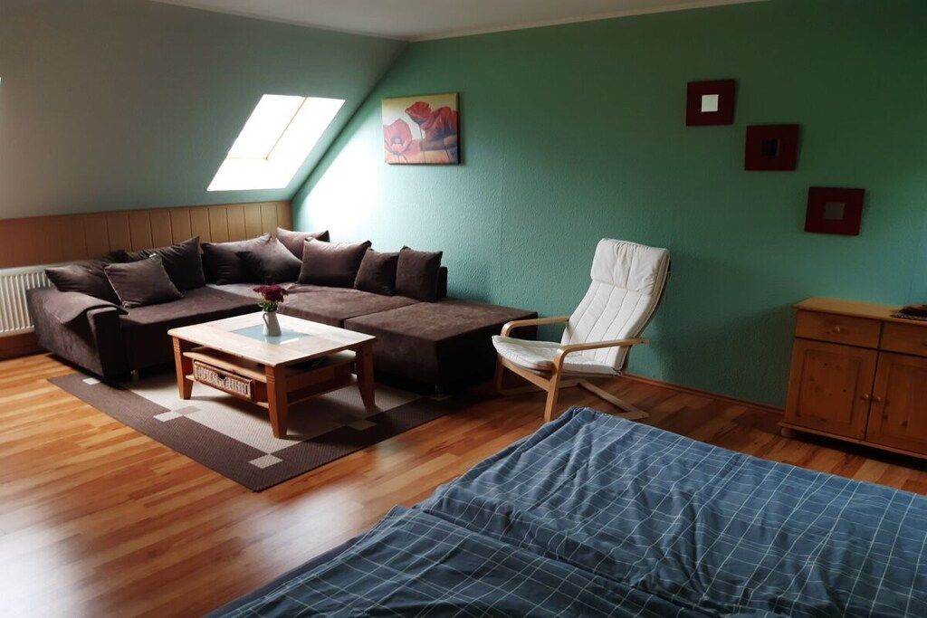 A cozy living room with a sectional sofa, a wooden coffee table, a white armchair, and a blue bedspread.