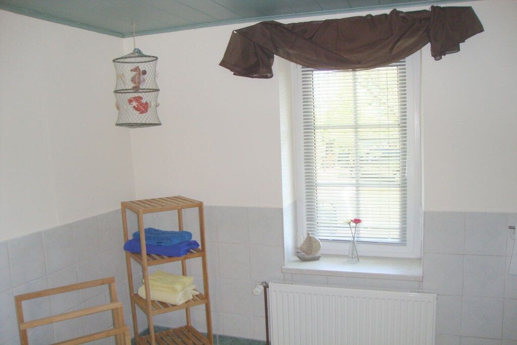 A bathroom with a window, a radiator, a wooden shelf, and a hanging birdcage.