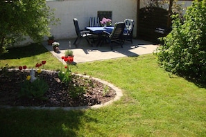 A patio with a table and chairs, surrounded by a garden with flowers and a lawn. - Holiday apartment in Jabel with swimming pool (Jabel)