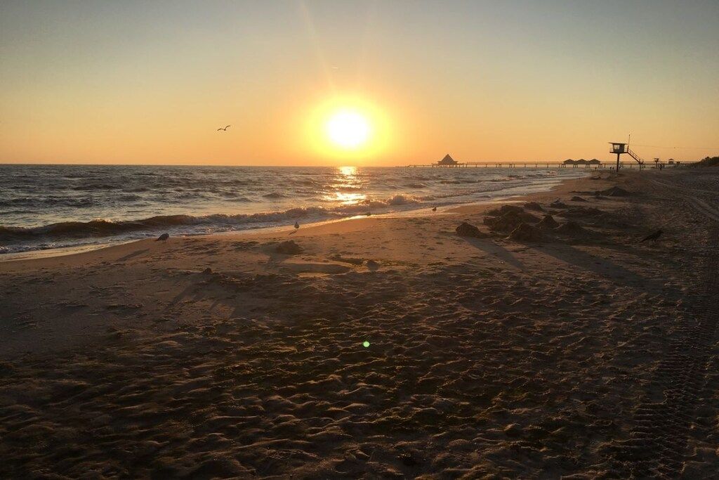 A beach with a sunset, waves, and a lifeguard tower.