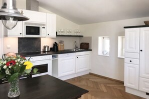 A modern kitchen with white cabinets, a microwave, a sink, and a dining area with a dark table. - Villa Achterkerke / upper floor south & sea (Seebad Heringsdorf)