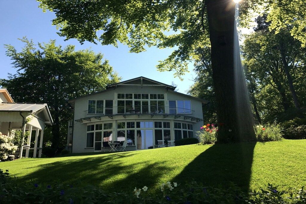 Een gebouw met twee verdiepingen en een balkon, omringd door weelderige begroeiing en een verzorgd gazon.