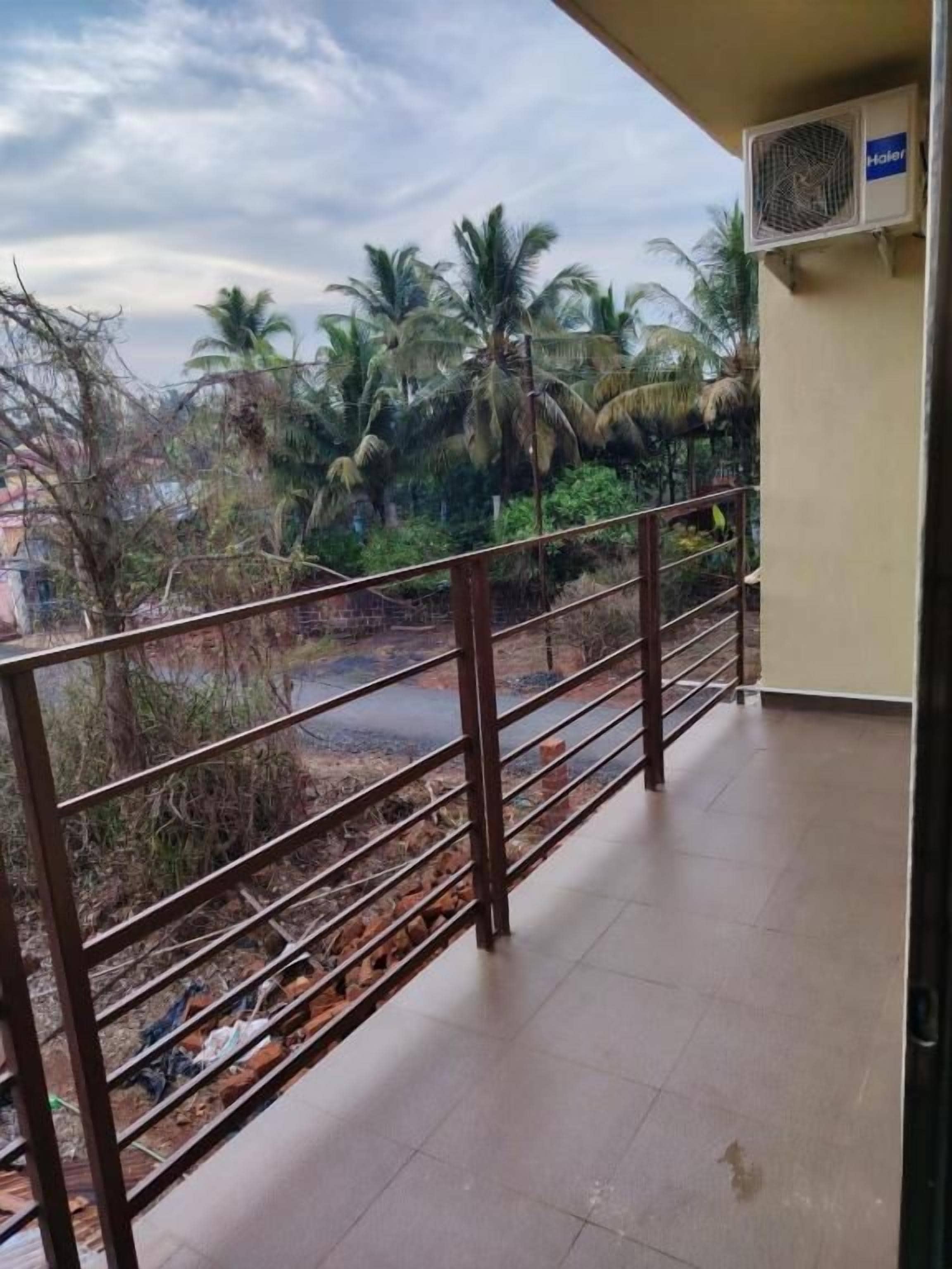 A balcony with a metal railing overlooking a garden with palm trees and a paved area.