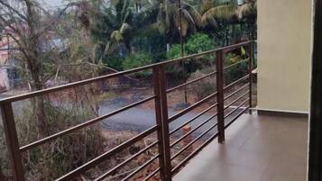 A balcony with a metal railing overlooking a garden with palm trees and a paved area.
