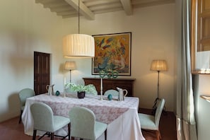 Comedor con una mesa dispuesta para cuatro personas, rodeada de sillas, una araña y una chimenea con un cuadro encima.