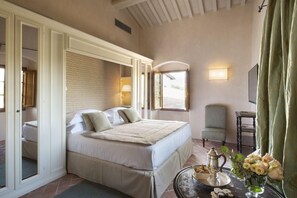 A hotel room with a large bed, a chair, a table with a tray of breakfast items, and a vase of flowers.