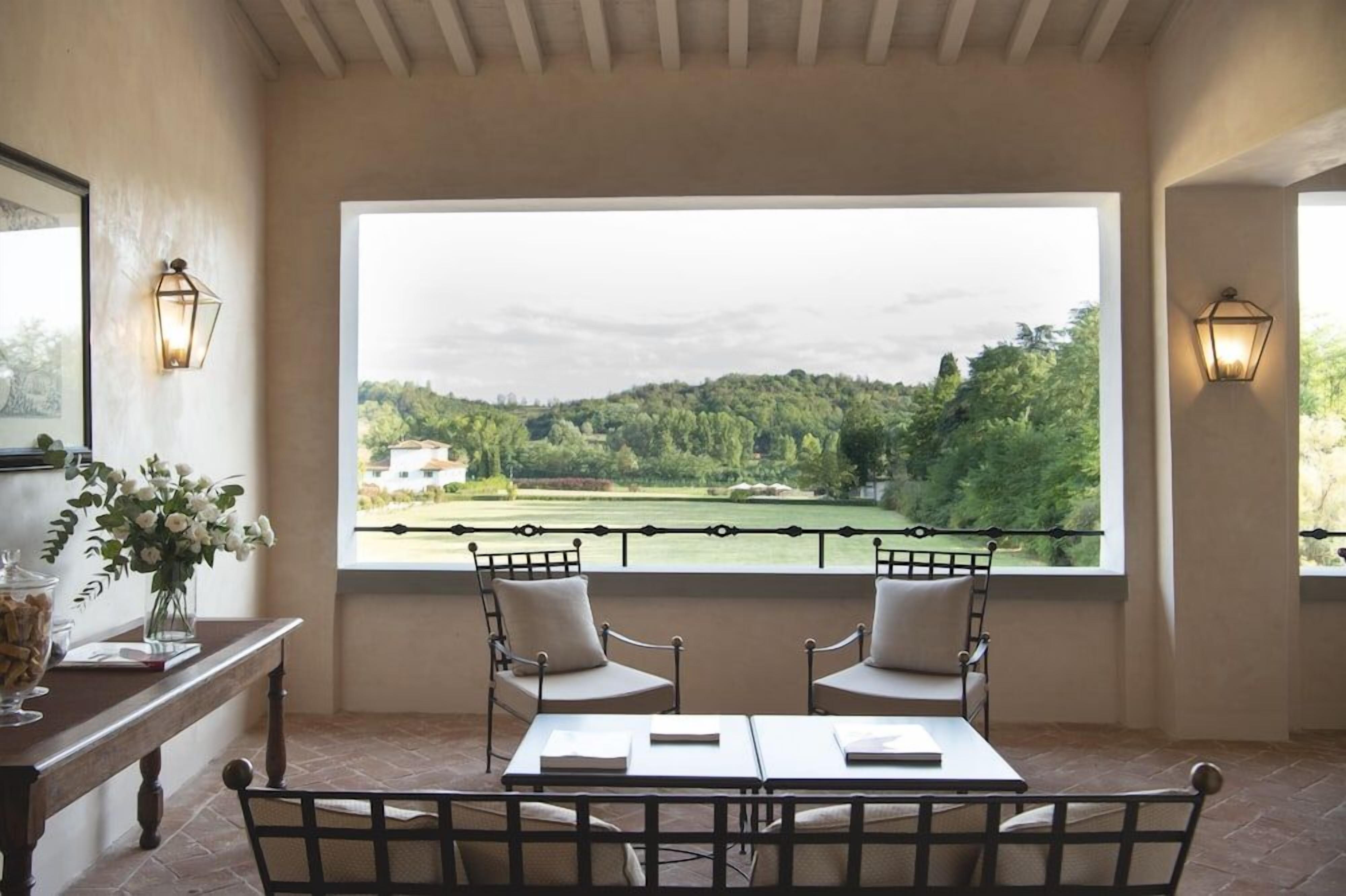 Una habitación con un ventanal amplio que da a un paisaje, dos sillones, una mesa y luces en la pared.