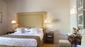 A hotel room with a large bed, two bedside tables with lamps, a small table with a vase of flowers, and framed pictures on the wall.