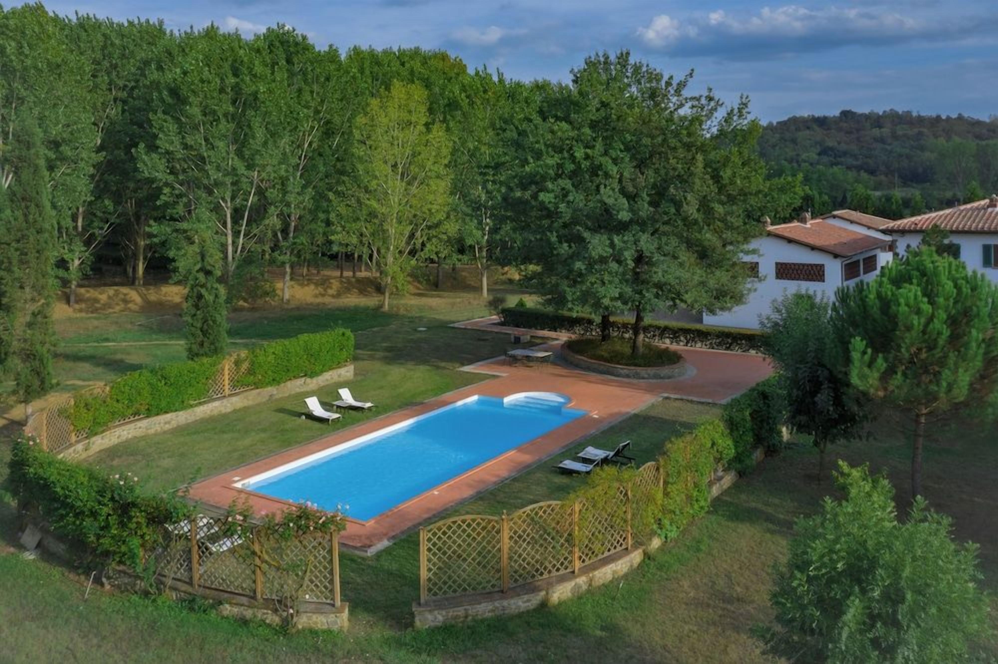 A residential property with a swimming pool, surrounded by a fenced yard and trees.