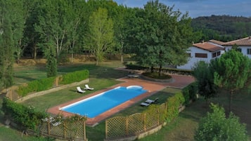 A residential property with a swimming pool, surrounded by a fenced yard and trees.