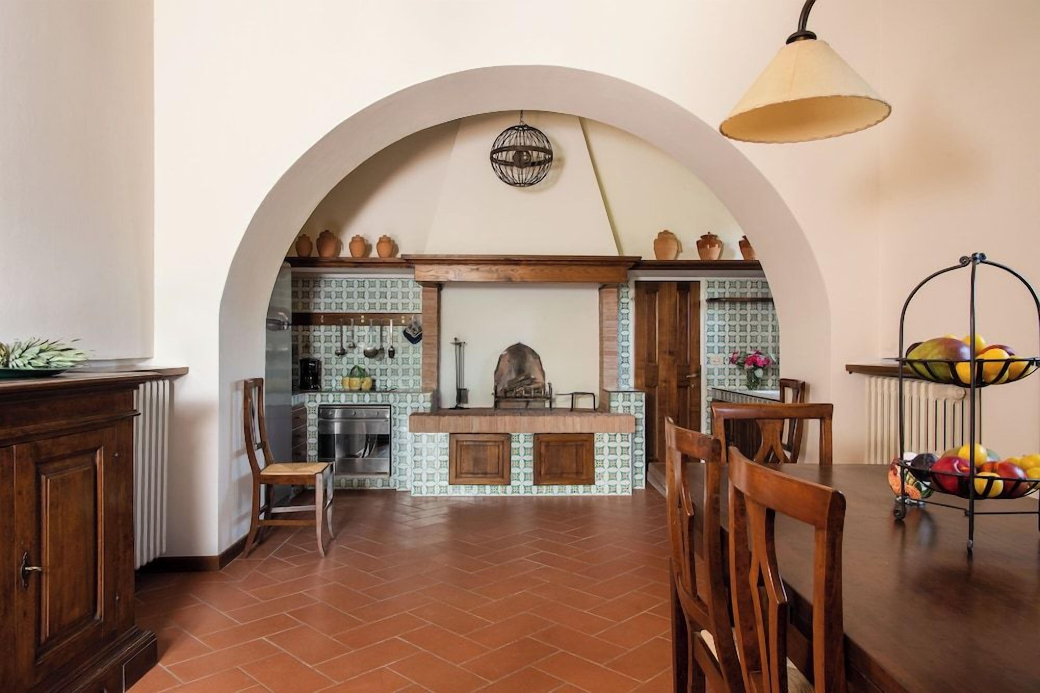 Una cocina con un arco, una lámpara colgante y un frutero sobre un pedestal.