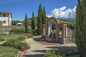 A garden with a fountain, a white building, and tall cypress trees. - Viesca Suites & Villas Il Borro Toscana (Reggello)